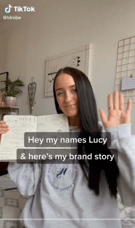 Lucy Parker smiles and waves at camera with text "Hey my names Lucy and here's my brand story" overlaid